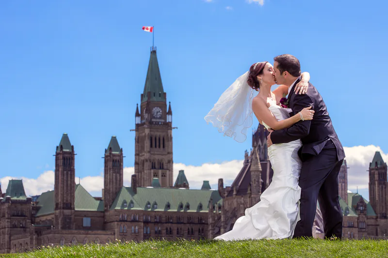 A couple kiss in front of Canada's Parliament Hill during their wedding day. A wedding photo by Jeffrey Meyer.