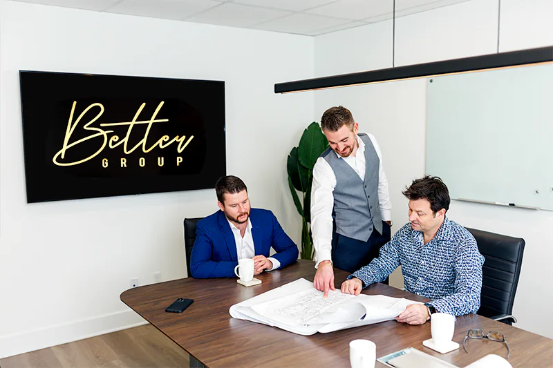 Three business partners review building plans during their team meeting. A commercial photo by Jeffrey Meyer.