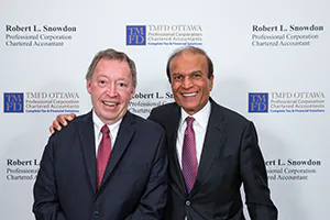 Two business friends embrace in front of their media wall.   Event photo by Jeffrey Meyer.