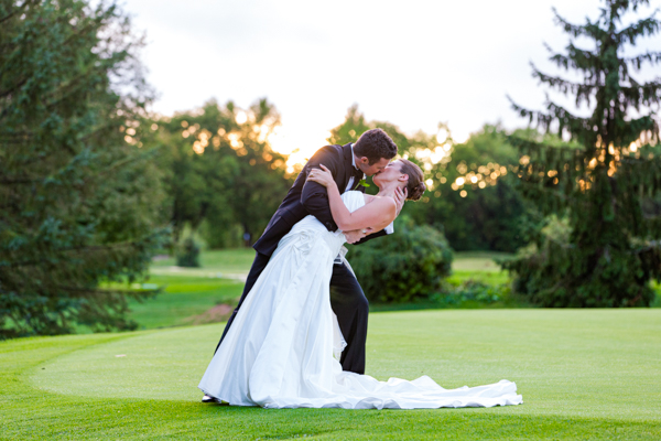A groom dips and kisses his wife on a golf course