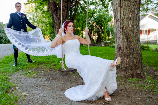 A bride swings from a tree, with her groom holding her veil